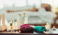 A woman relaxes at a spa. In the foregroun, a towel, candles and various other wellness items sit on a table.