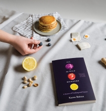 A copy of "All the Wild Hungers" by Karen Babine is surrounded by tea, pancakes and other fall foods.