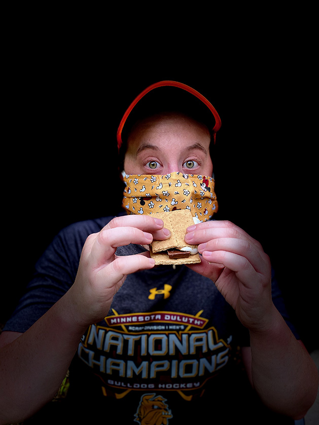 A man wearing a protective mask holds a s'more.